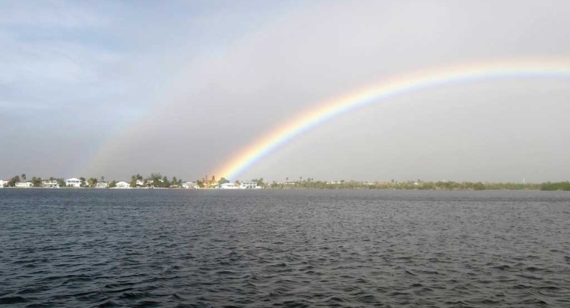 A rainbow reaches over a body of water to a piece of land in the distance. 